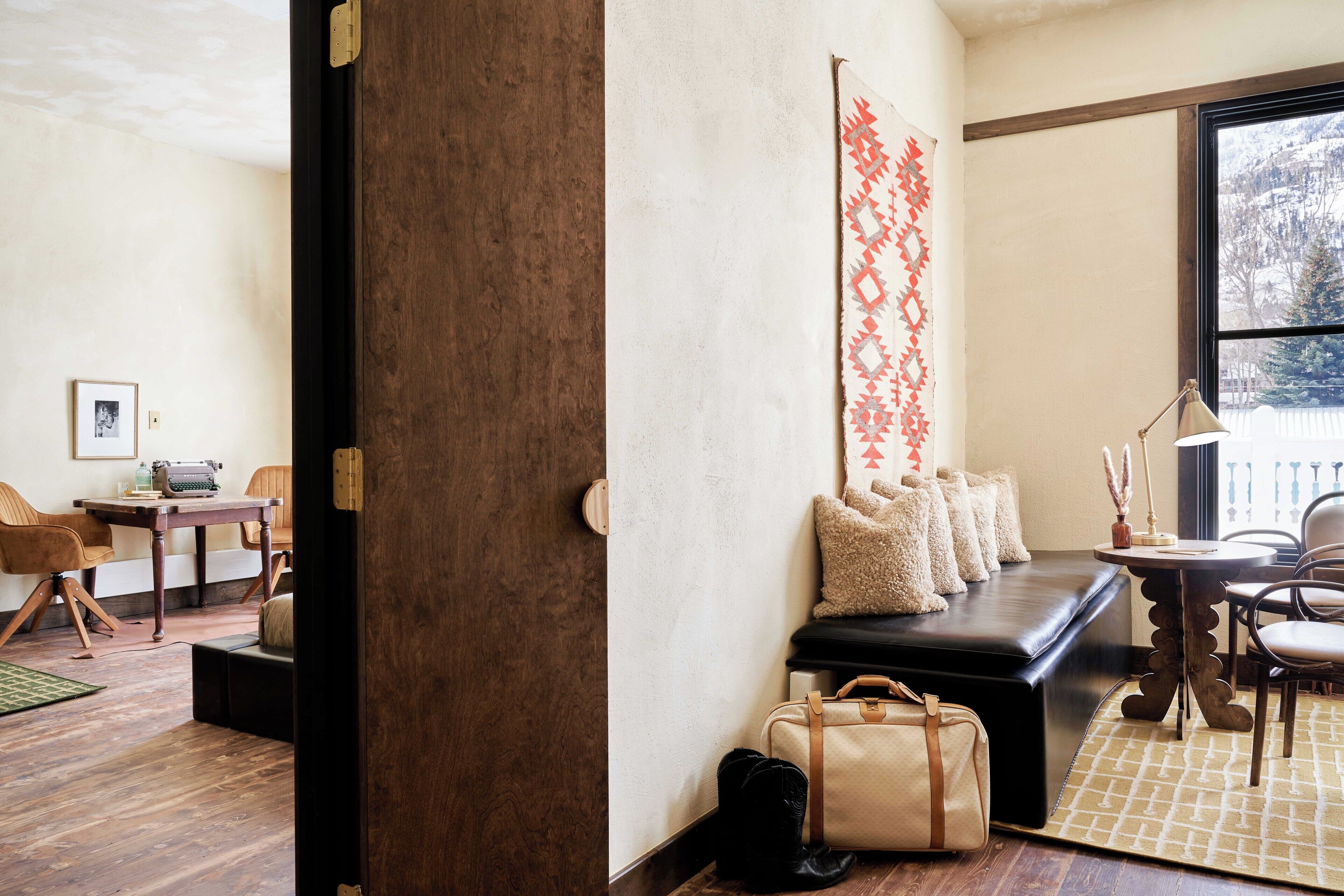 A cozy living room with a dark brown door, a black leather sofa, a patterned rug, and a wooden coffee table.