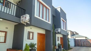 A modern residential building with a grey facade, wooden doors, and air conditioning units. - Grayville Apartments #5 (Lusaka)