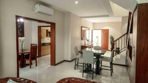 A spacious living area with a dining table, a leather sofa, and a staircase leading to an upper floor. - Grayville Apartments #5 (Lusaka)