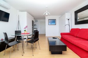 A modern living room with a red sofa, a glass coffee table, and a dining area with a glass table and chairs. - Renovated studio in Elviria, fantastic sea views (Marbella)
