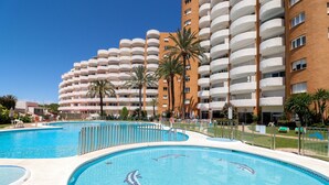A hotel with multiple balconies, a swimming pool with dolphin designs, and palm trees.