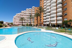 Un hotel con varios balcones, una piscina con diseños de delfines y palmeras.