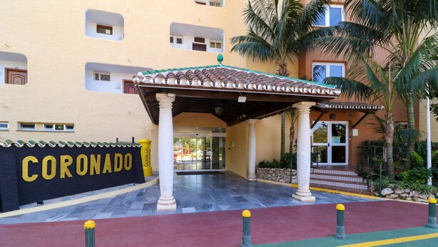 A hotel entrance with a covered patio, a sign reading "CORONADO," and a tiled walkway.