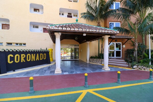 Entrada de hotel con un porche cubierto, un letrero que dice "CORONADO" y un camino empedrado.