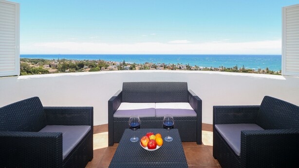A balcony with wicker furniture, a fruit bowl, and wine glasses. - Renovated studio in Elviria, fantastic sea views (Marbella)