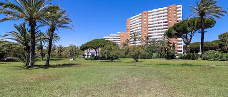 A large, multi-story building with balconies, surrounded by a well-maintained grassy area with palm trees.