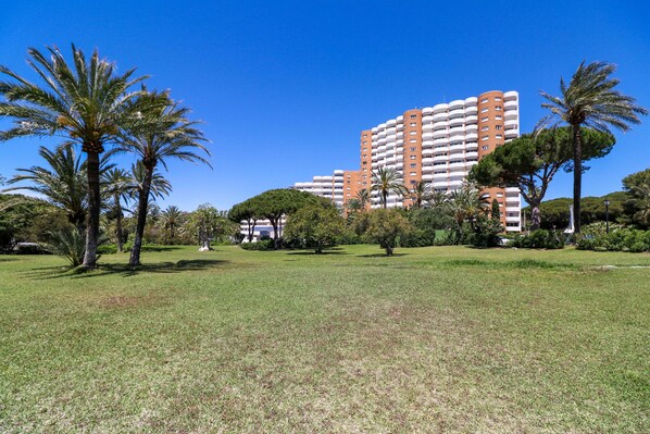 A large, multi-story building with balconies, surrounded by a well-maintained grassy area with palm trees. - Renovated studio in Elviria, fantastic sea views (Marbella)
