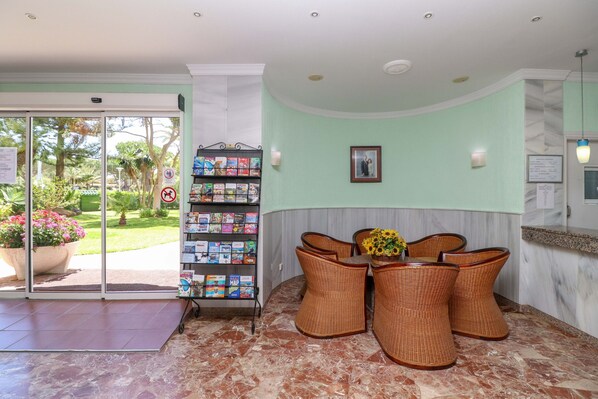 A reception area with a glass door leading to a garden, wicker chairs, a small table with a vase, and a bookshelf with magazines. - Renovated studio in Elviria, fantastic sea views (Marbella)
