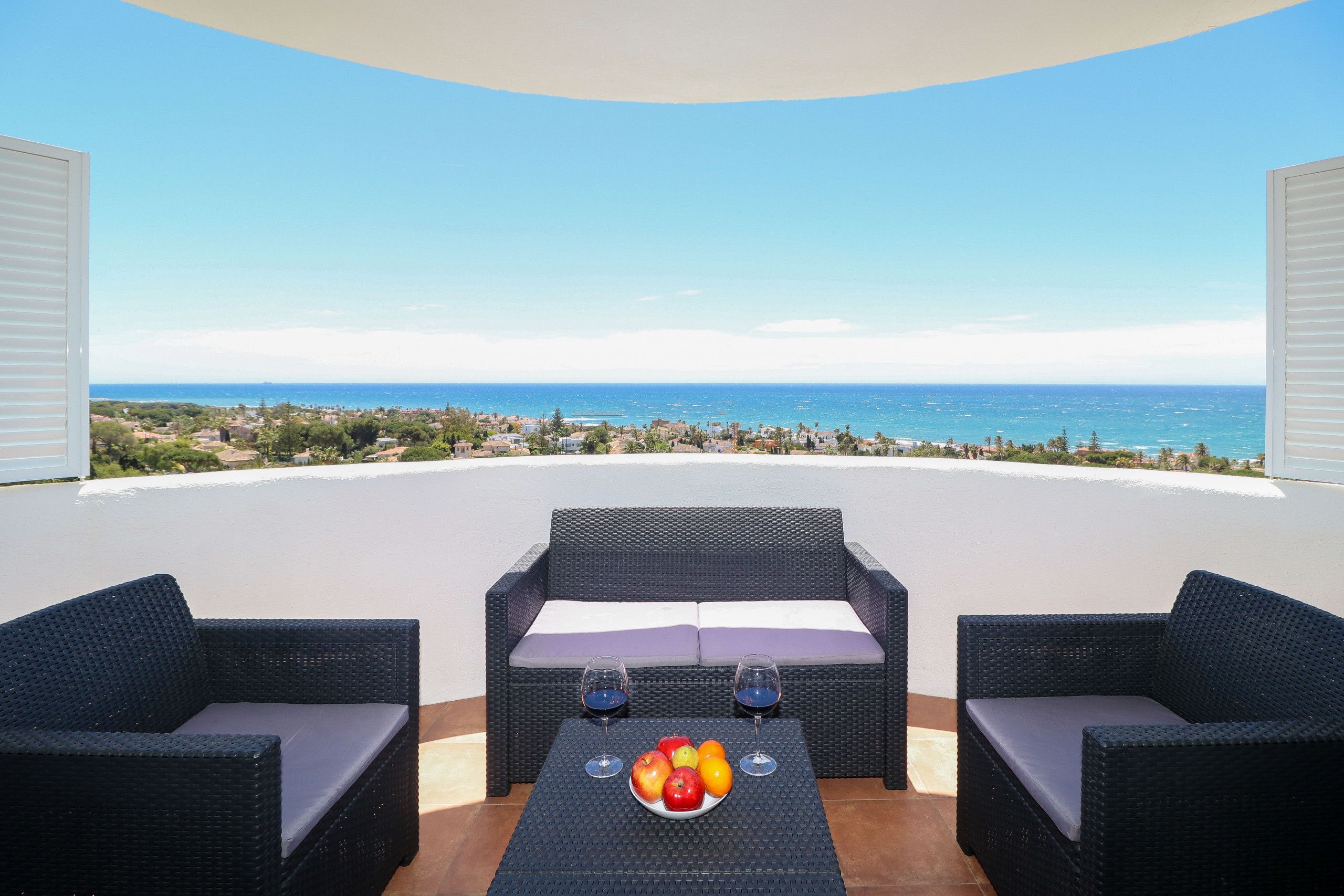 A balcony with wicker furniture, a fruit bowl, and wine glasses.