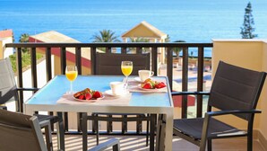 Una mesa con alimentos y bebidas para el desayuno en un balcón con vistas al mar.