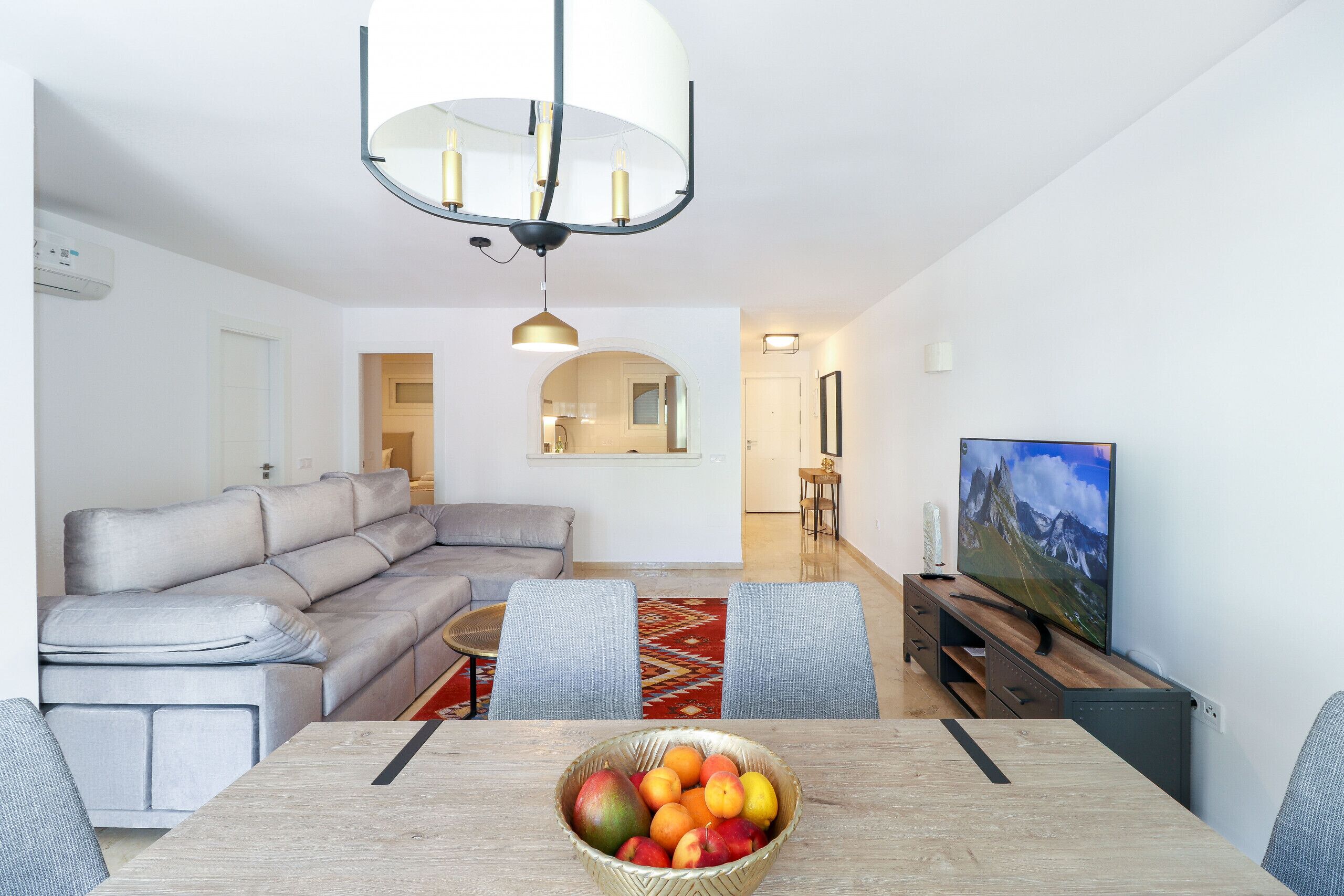 Una sala de estar moderna con un sofá, televisor y una mesa de comedor con frutero.