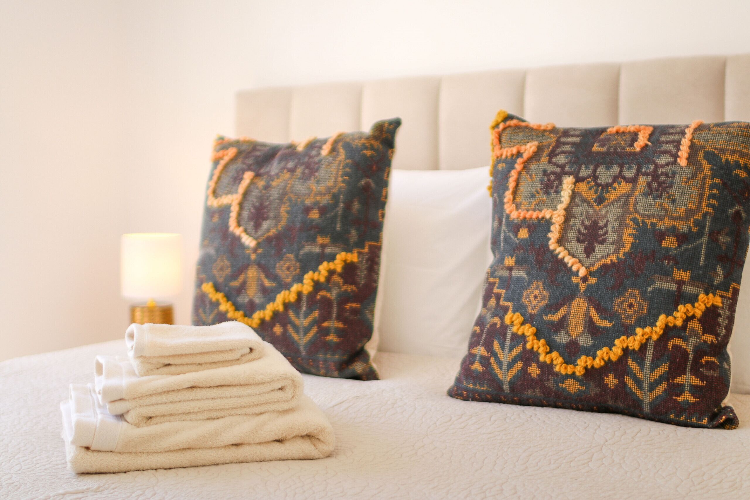 Una cama bien tendida, con toallas blancas dobladas y dos almohadas estampadas.