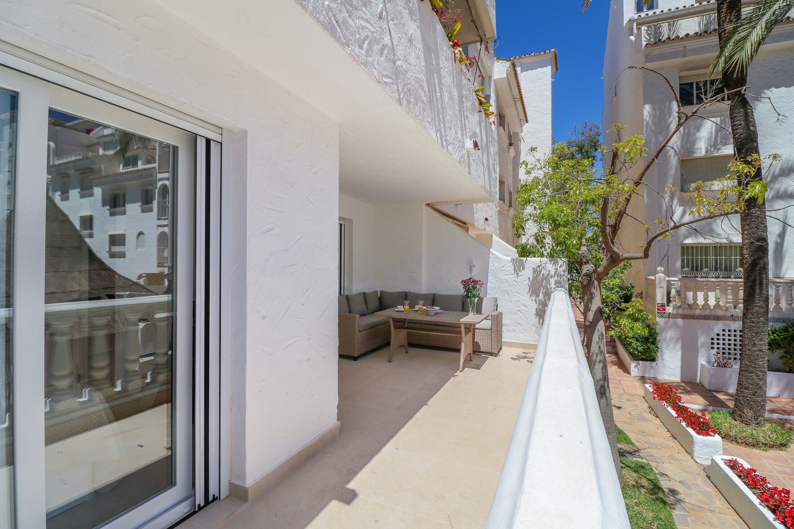 Un balcon avec un canapé et une table, une porte vitrée et une rambarde blanche.