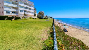 Un hotel fronte spiaggia con un prato, una piscina e una spiaggia con ombrelloni.
