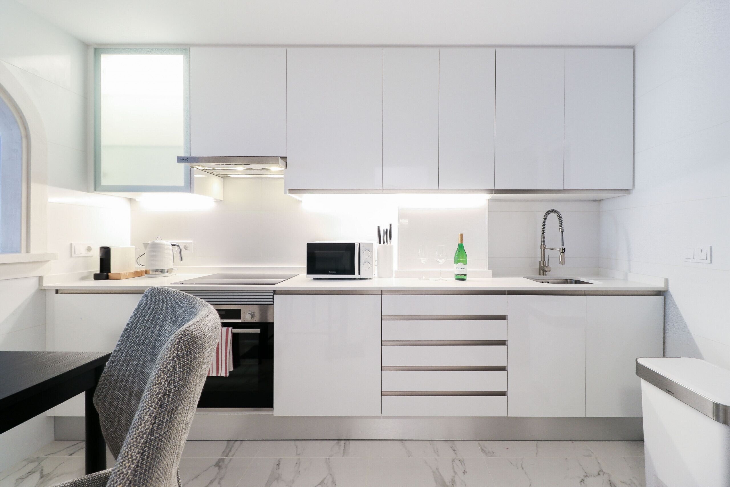 A modern kitchen with white cabinetry, a microwave, a sink, and a window above the counter.