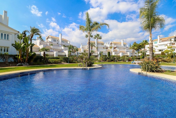 A swimming pool surrounded by palm trees and white buildings with red roofs.