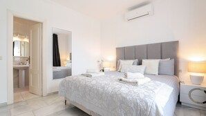 Un dormitorio moderno con una cama grande, lámparas de noche, un espejo y un baño visible a través de una puerta abierta.