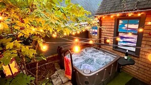Un jacuzzi en un jardín con luces colgantes, un muro de piedra y un edificio de ladrillo con una ventana.