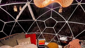 Un interior acogedor de diseño geométrico, con una zona de estar central, una mesa con un cuenco y una lámpara colgante.