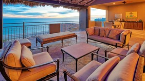 A balcony with seating, a table, and a view of the ocean.