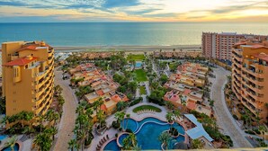 A resort with multiple buildings, a central pool area, and a beach view.