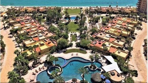 A resort with a central pool, multiple buildings, and a beach.