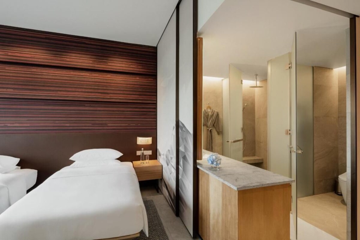 Una habitación de hotel con cama, mesita de noche, lámpara y baño con ducha e inodoro.