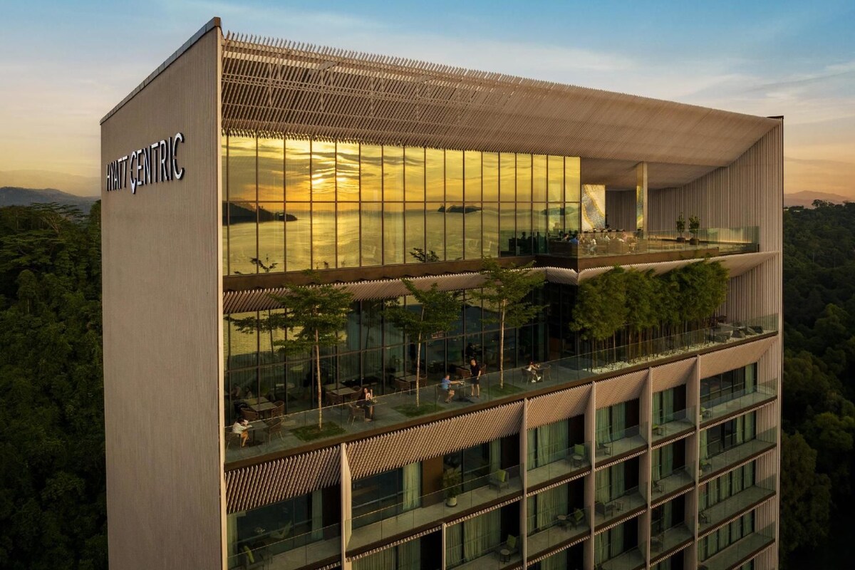 Un hotel moderno con fachada de vidrio, varios balcones y vistas del paisaje circundante.
