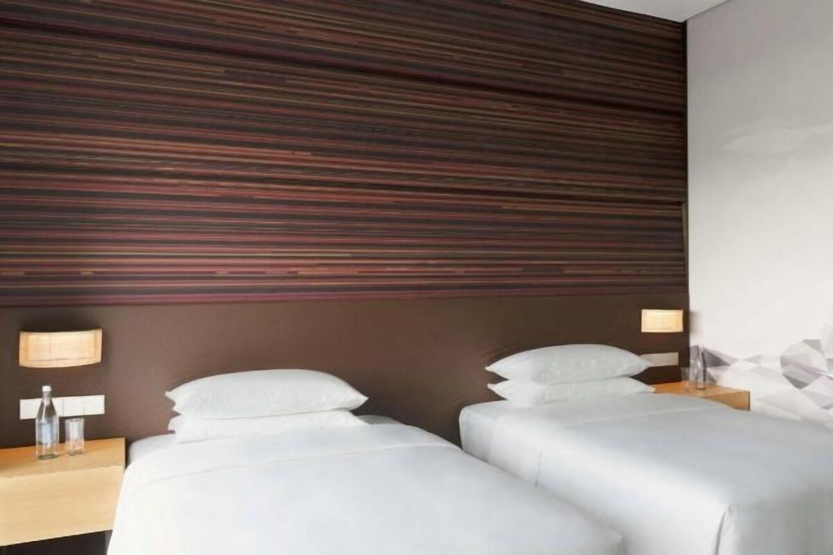 Habitación de hotel con dos camas, cabecera de madera y una obra de arte mural con motivos geométricos.