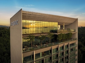 A modern hotel with a glass facade, multiple balconies, and a view of the surrounding forest. - Hyatt Centric Kota Kinabalu (Kota Kinabalu)