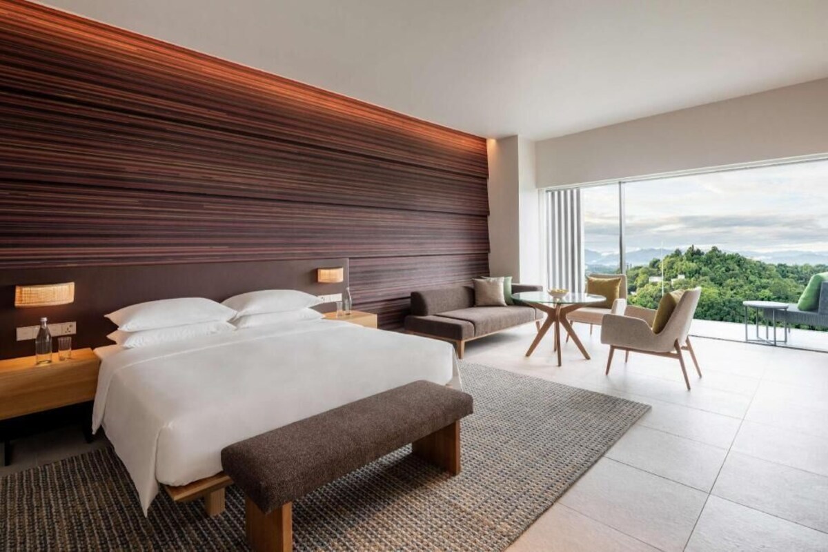 Habitación de hotel moderna con una cama grande, un sofá, una mesita y vistas al exterior.