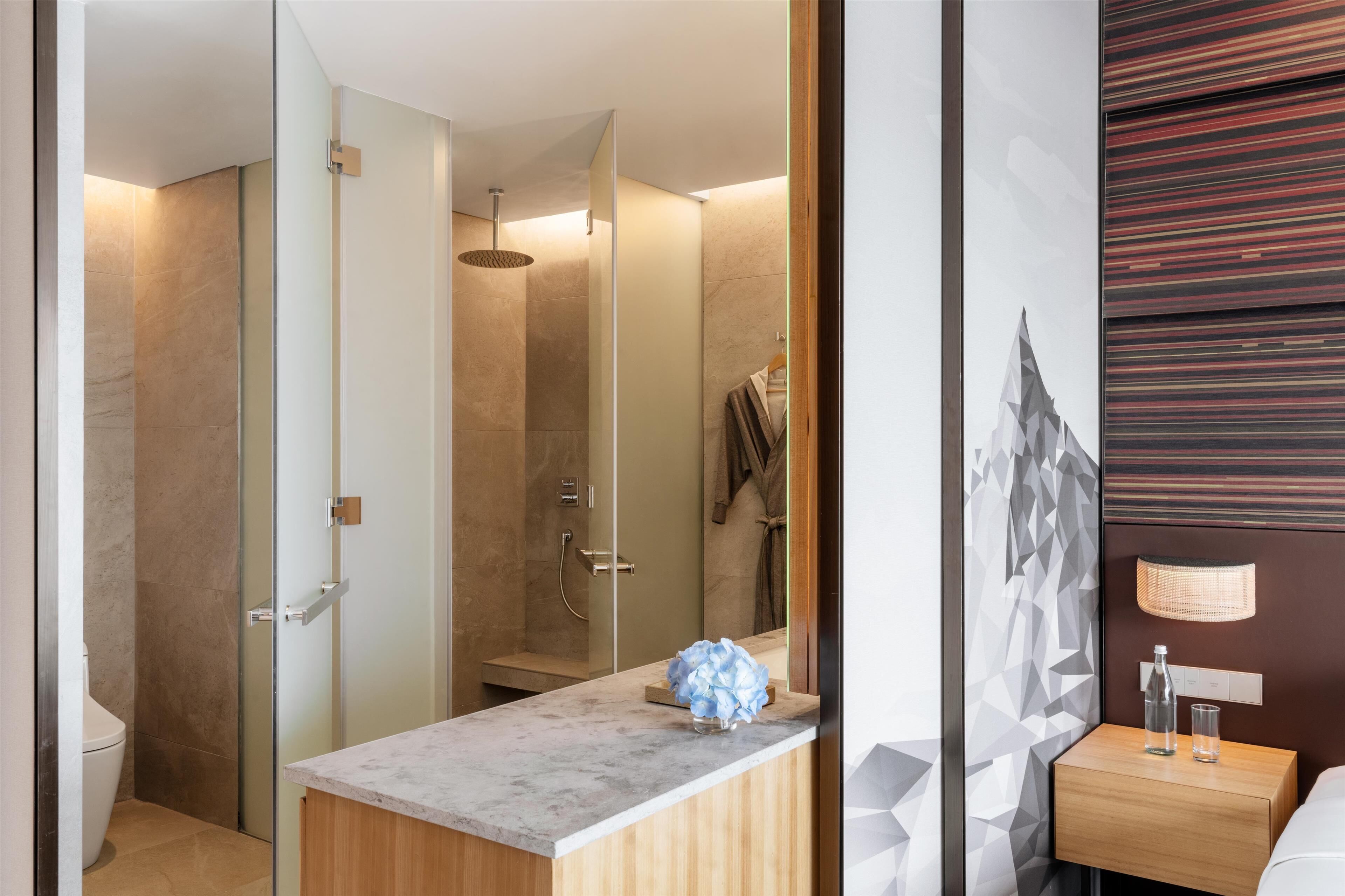 Un baño moderno con cabina de ducha de vidrio, lavabo de mármol y tocador de madera.