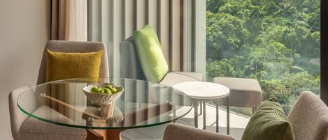 Una sala de estar moderna con una mesa de vidrio, dos sillas y vistas a un paisaje verde y exuberante a través de amplios ventanales.