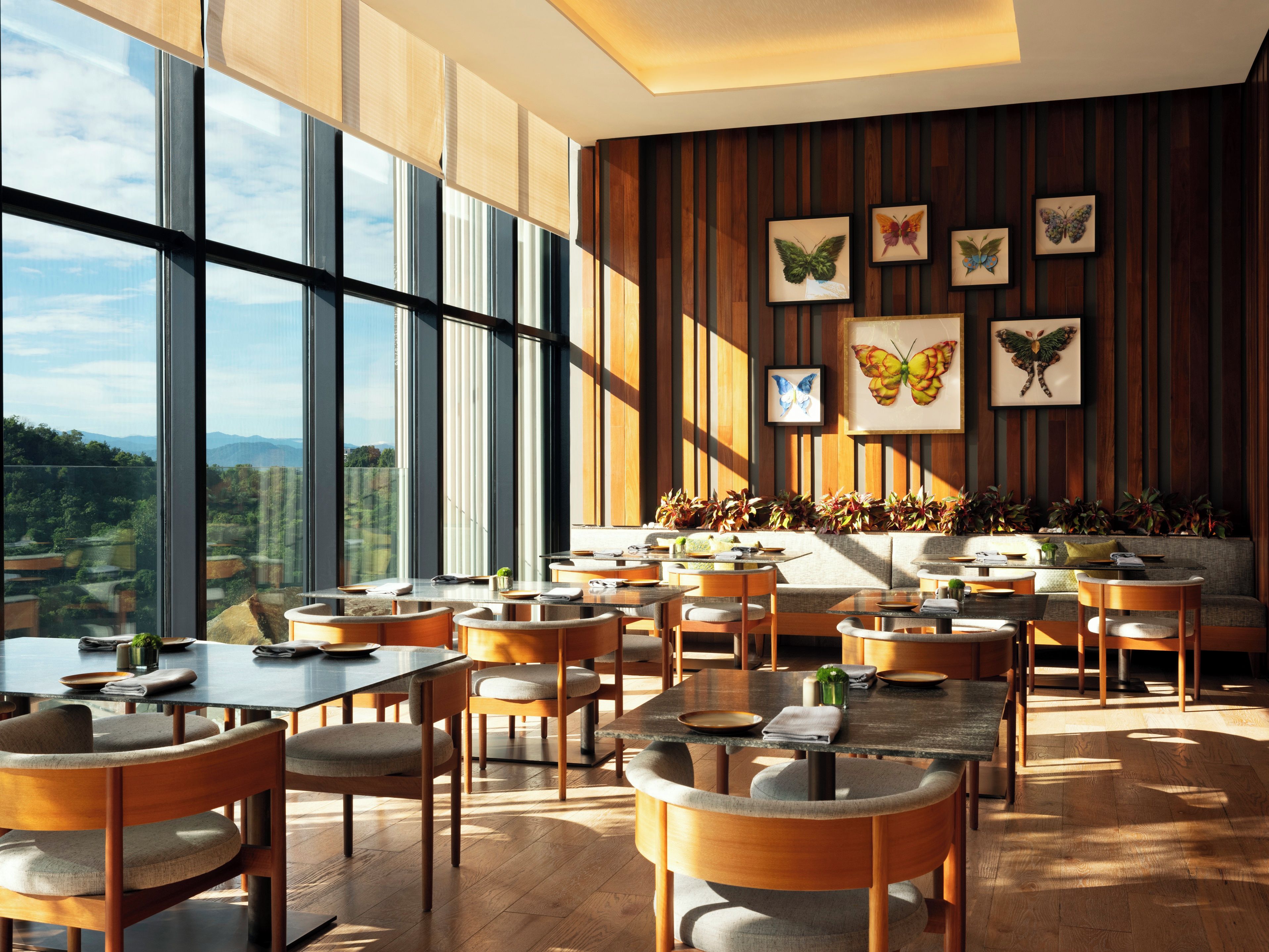 A modern dining area with large windows, wooden panel walls, and butterfly artwork.