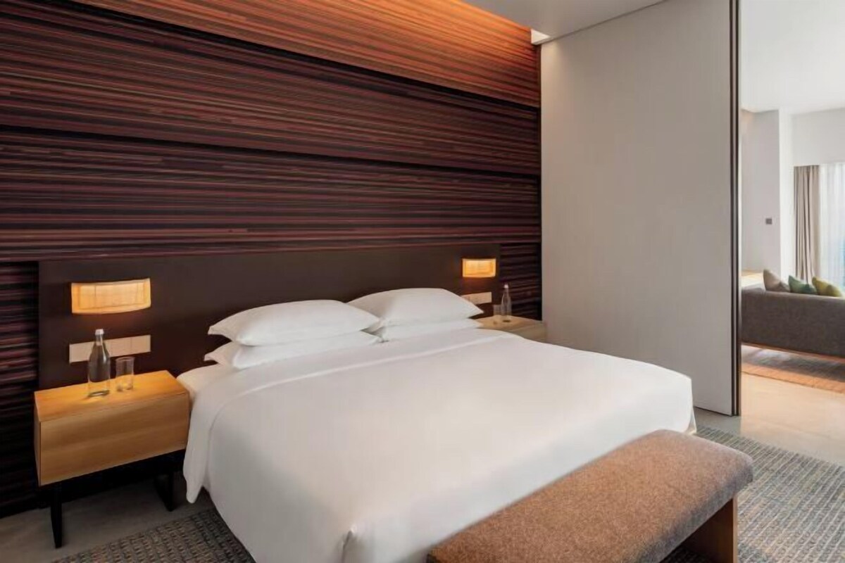 Una habitación de hotel moderna con una cama grande, cabecera de madera, lámparas de noche y un banco.