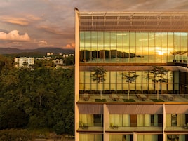 Un edificio moderno con varios pisos, amplias ventanas y una zona de balcón con mobiliario exterior.