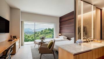 Ett modernt hotellrum med ett stort fönster, ett skrivbord, en stol, en säng, ett badrum med en spegel och en TV.