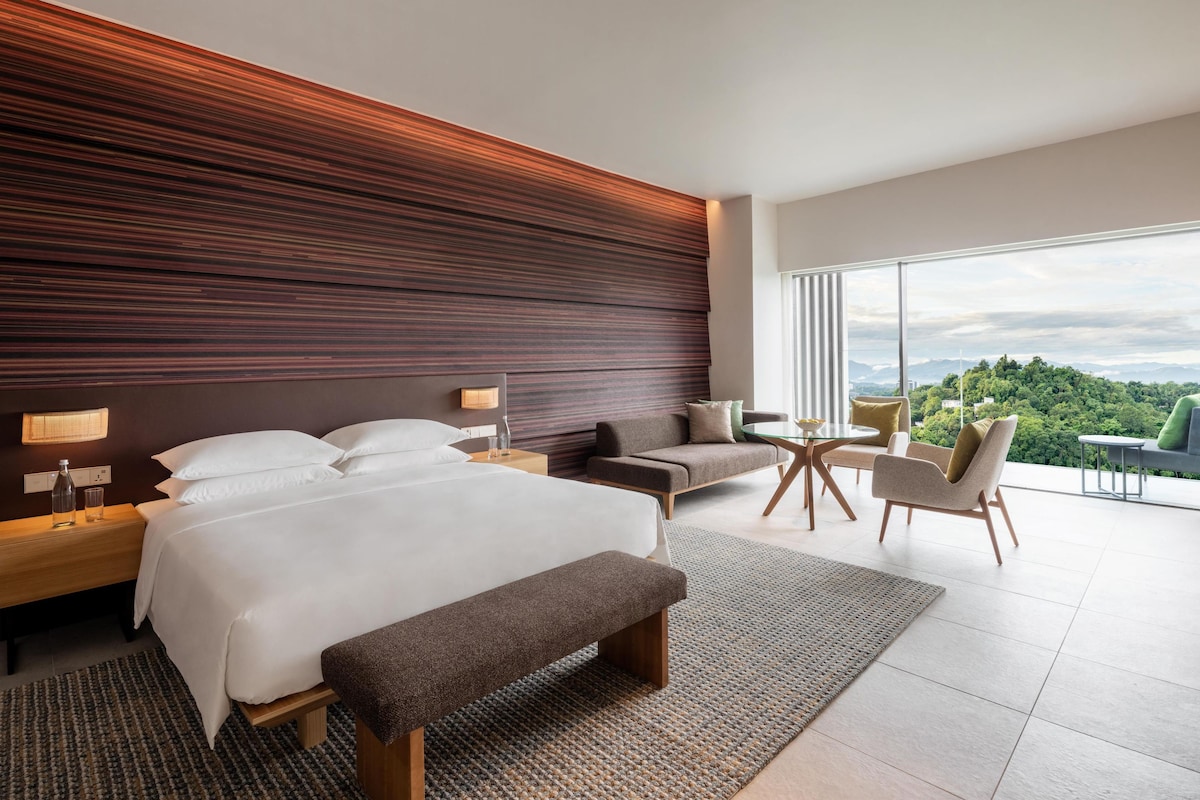 Habitación de hotel moderna con una cama grande, un sofá, una mesita y vistas al exterior.