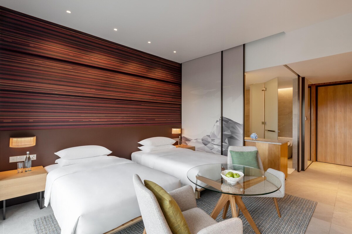 Una habitación de hotel moderna con una cama grande, un escritorio pequeño, una mesa de vidrio y un área de baño separada.