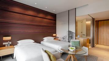 Une chambre d’hôtel moderne avec deux lits, une table à manger en verre et une salle de bain séparée.