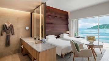 Ein modernes Hotelzimmer mit einem großen Bett, einem Schreibtisch mit Spiegel, einem kleinen Tisch und Blick aufs Meer.