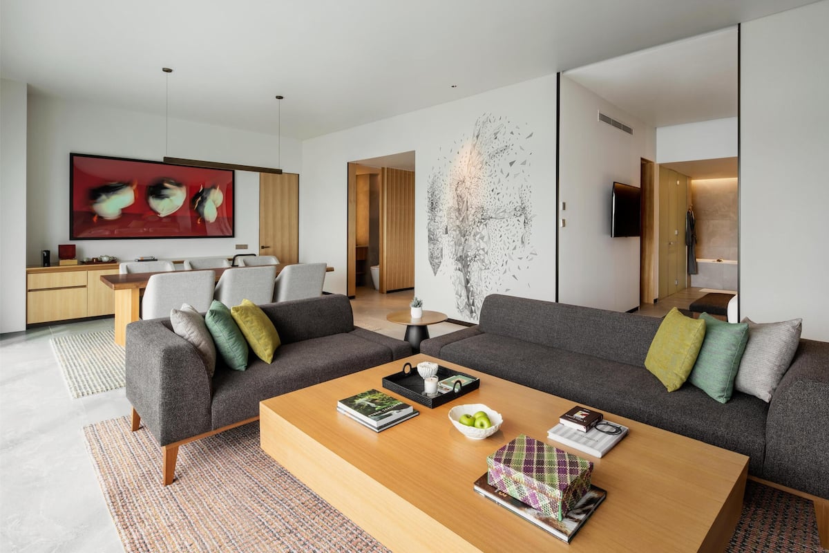 A modern living room with a sofa, coffee table, and artwork. There is a kitchen area with a dining table and chairs.