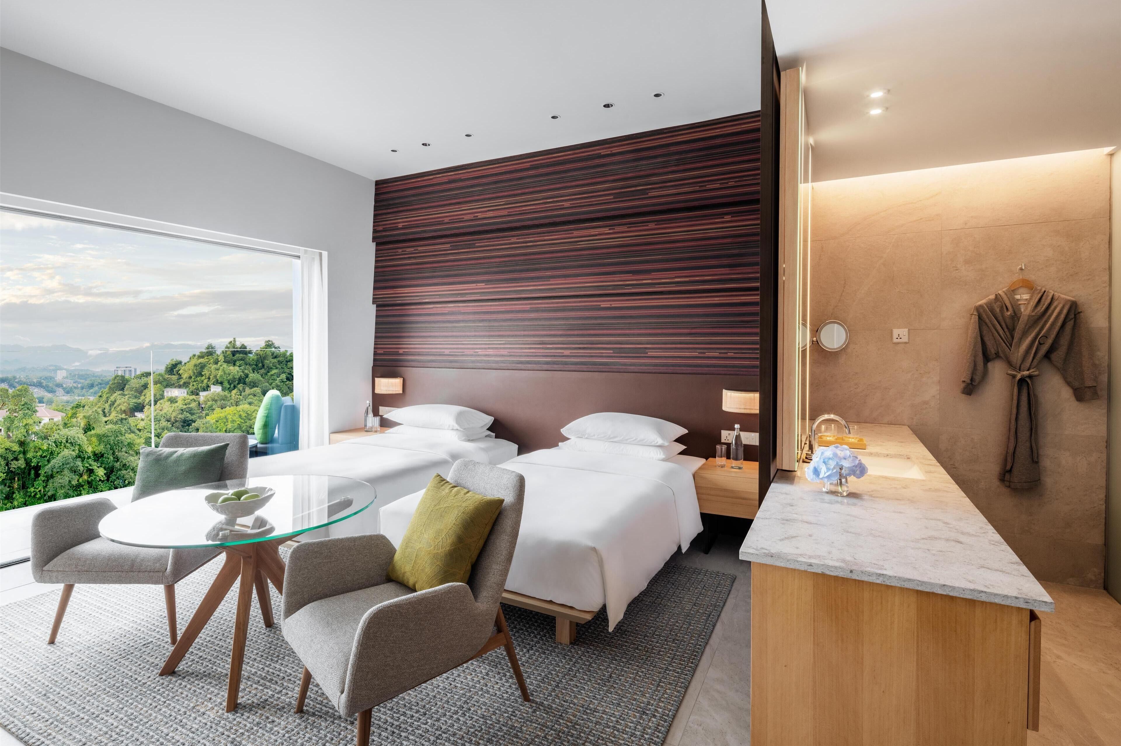 Habitación de hotel moderna con un ventanal grande, una mesa de comedor de cristal, dos camas, un escritorio de madera y vistas a la ciudad.