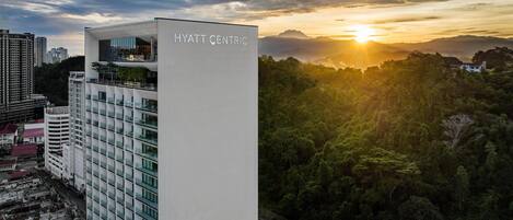 A modern Hyatt Centric hotel with a view of a sunset over a forested area.