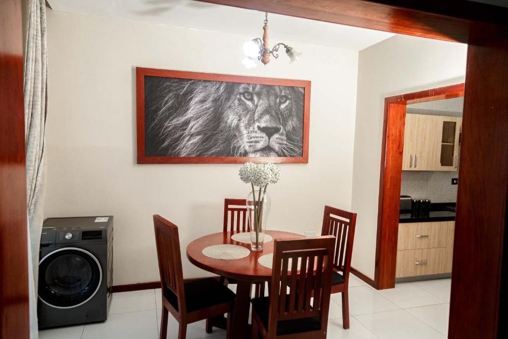 Un'area pranzo con un tavolo rotondo, quattro sedie di legno, un vaso con fiori e un quadro raffigurante il volto di un leone appeso al muro.