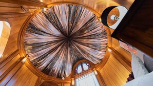 Una ventana redonda de vitral con diseño radial, vigas de madera y un pequeño reloj.