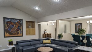 Una sala de estar moderna con un sofá seccional de cuero oscuro, una mesa de centro redonda de madera y una alfombra estampada.