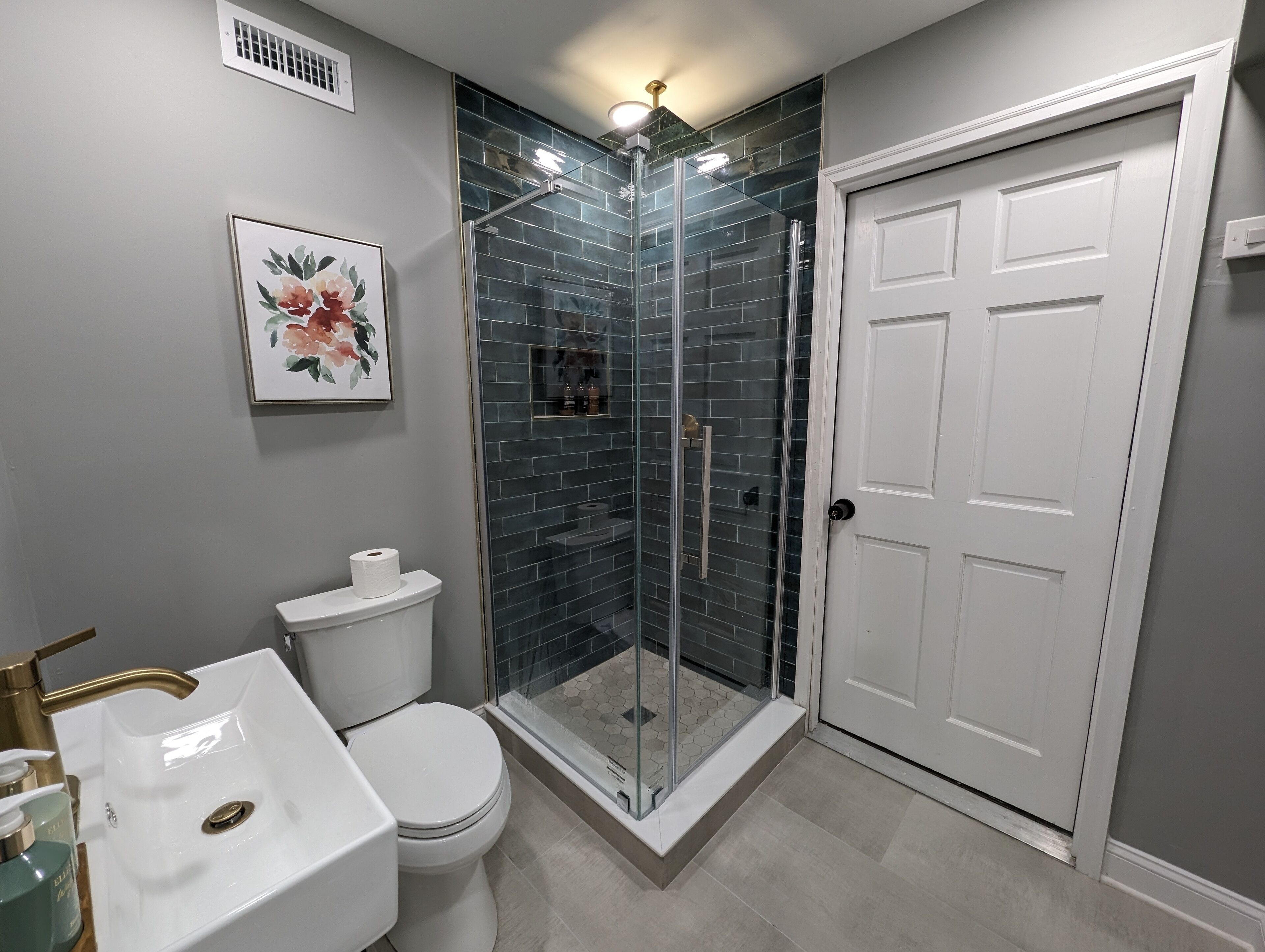 A bathroom with a white toilet, a white sink, a glass shower enclosure, and a white door.