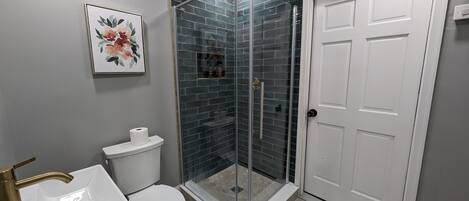 A bathroom with a white toilet, a white sink, a glass shower enclosure, and a white door.