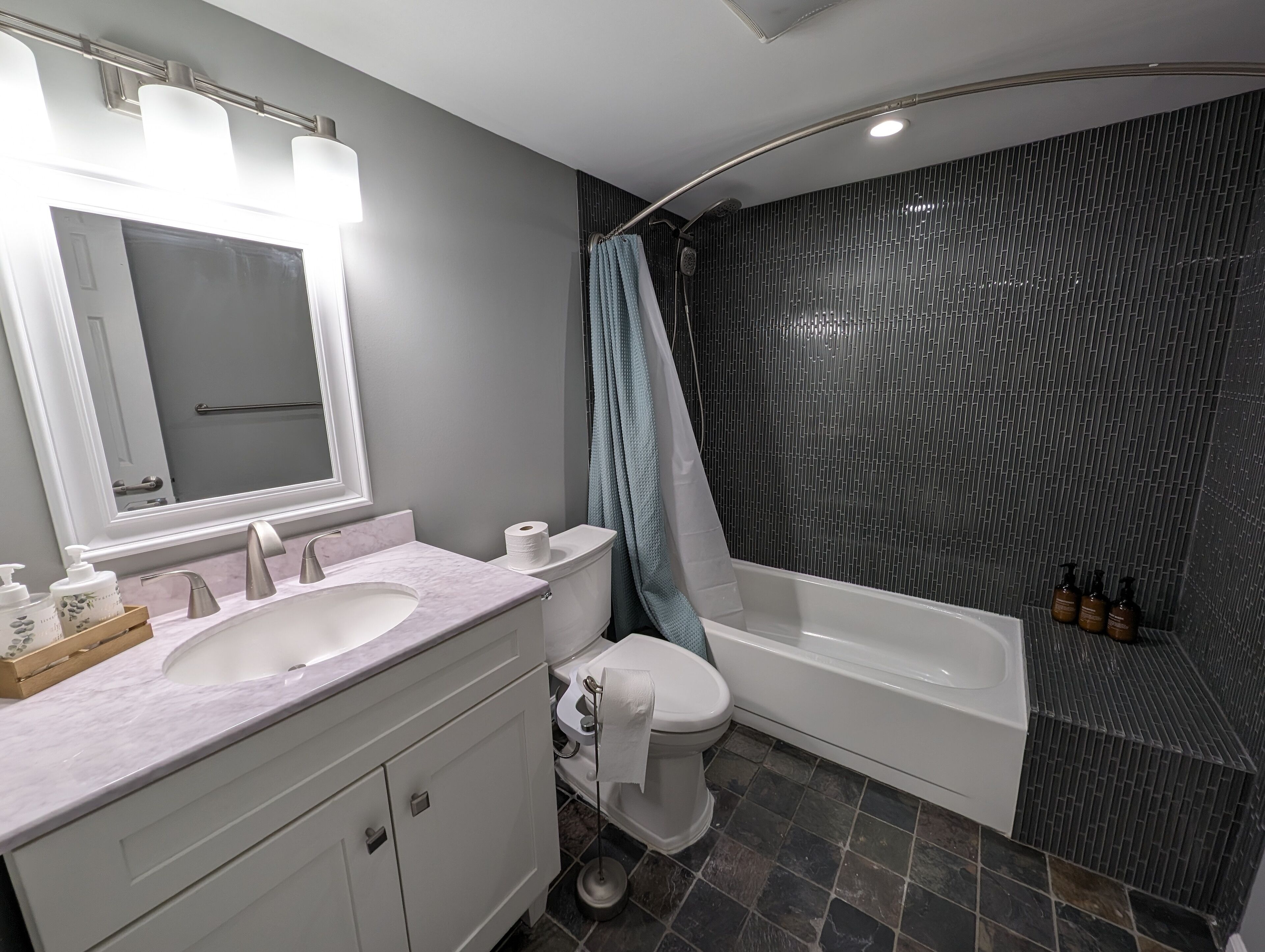 A modern bathroom with a white vanity, a large mirror, a bathtub, and a shower area.